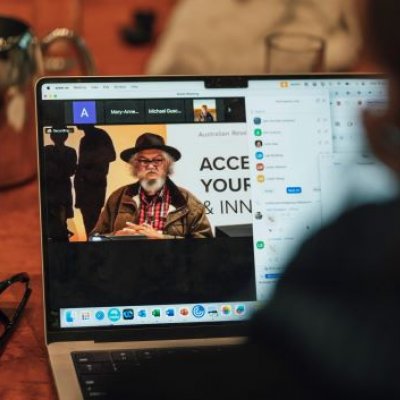 An image showing a laptop screen over a person's shoulder, with an Indigenous Australian on the screen.